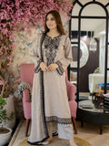 Woman in an embroidered outfit standing in a decorated room with pink flowers and a mirror.